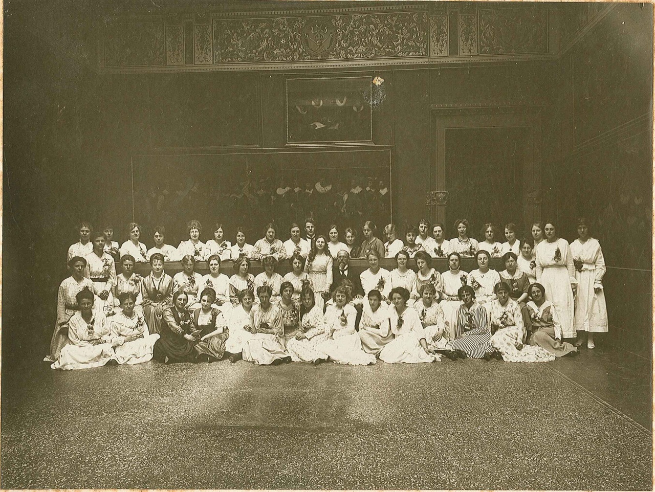 Foto van een groep van ruim 50 in het wit geklede dames met in hun midden een oudere man in jacquet.