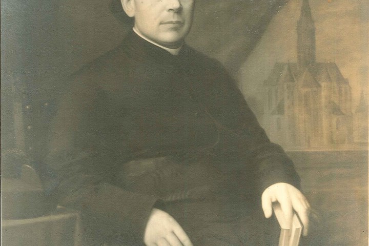 Foto van een priester met op de achtergrond een schilderij van de Vondelkerk.