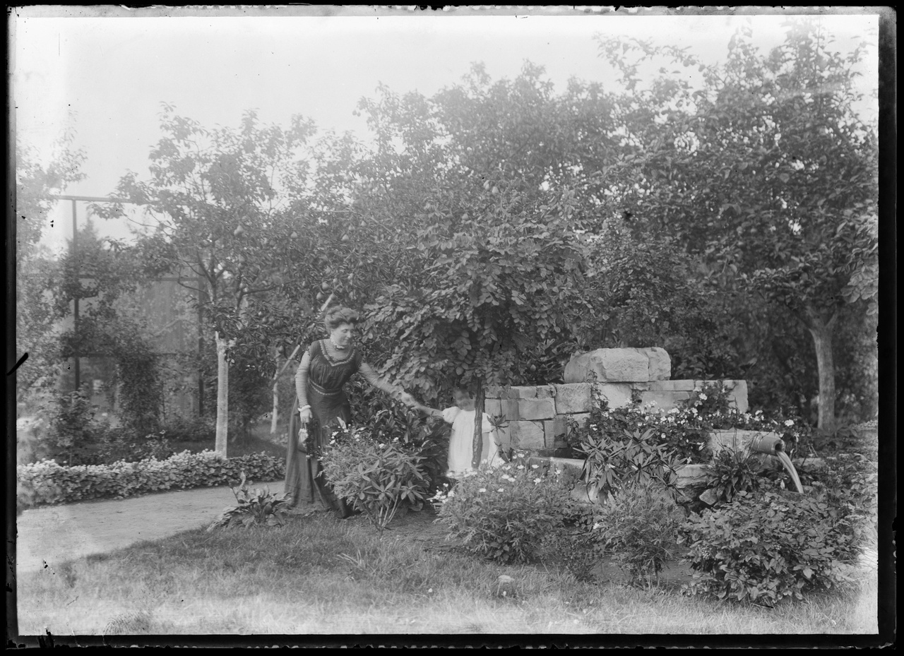 Glasnegatief van familiefoto waarop vrouw met kind in tuin