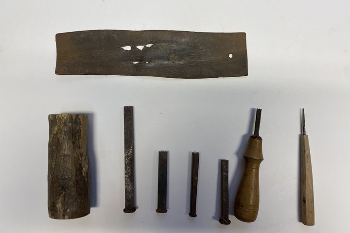 Vier stempels, een stempel met handvat, een priem (prikker), rond stukje hout en een leertje.